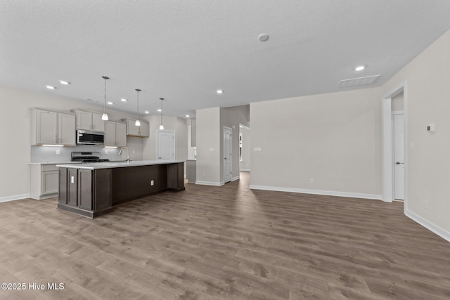 kitchen with appliances with stainless steel finishes, a sink, light countertops, open floor plan, and an island with sink