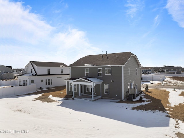 snow covered house featuring fence, a residential view, and cooling unit