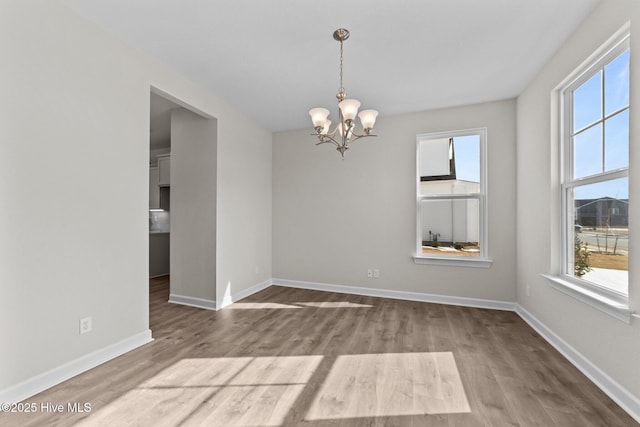 empty room with baseboards, a notable chandelier, plenty of natural light, and wood finished floors