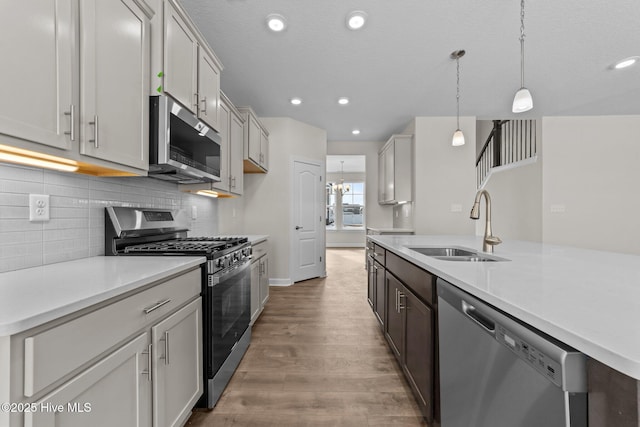 kitchen featuring wood finished floors, light countertops, a sink, appliances with stainless steel finishes, and backsplash