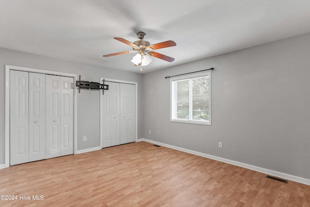 unfurnished bedroom featuring light hardwood / wood-style floors, two closets, and ceiling fan