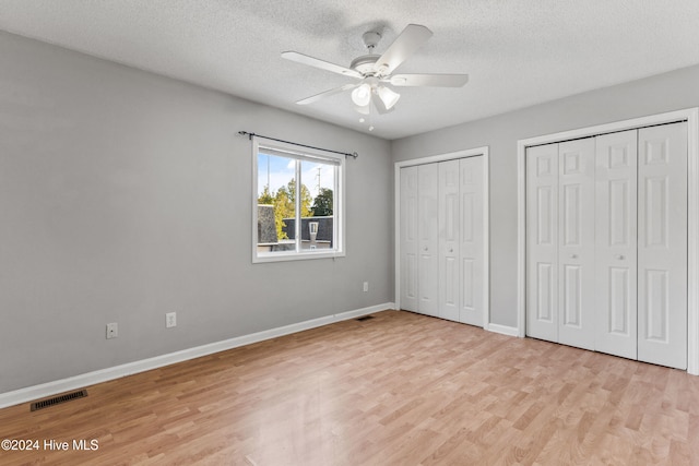 unfurnished bedroom featuring multiple closets, light wood-type flooring, a textured ceiling, and ceiling fan