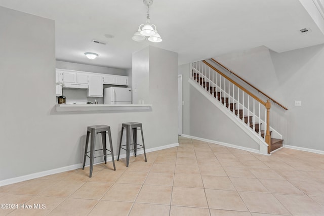 kitchen featuring white refrigerator, white cabinets, kitchen peninsula, a notable chandelier, and decorative light fixtures