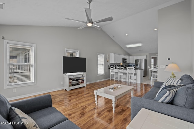 living room with visible vents, baseboards, vaulted ceiling, light wood-style floors, and a ceiling fan