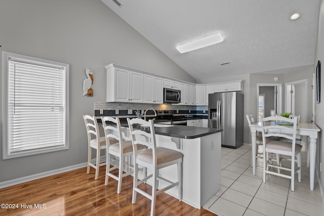 kitchen with a breakfast bar area, a peninsula, white cabinets, appliances with stainless steel finishes, and dark countertops