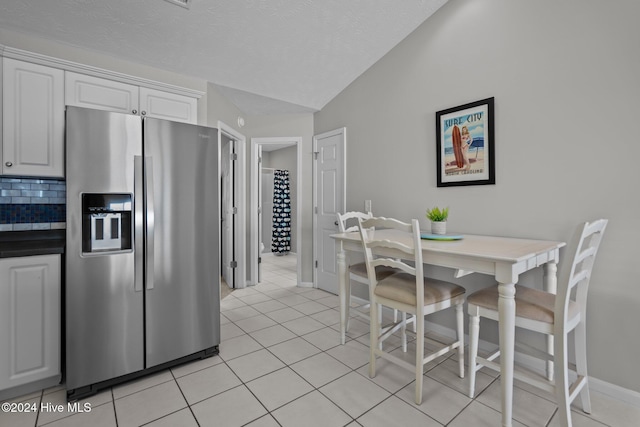 kitchen featuring stainless steel refrigerator with ice dispenser, backsplash, white cabinetry, light tile patterned floors, and lofted ceiling