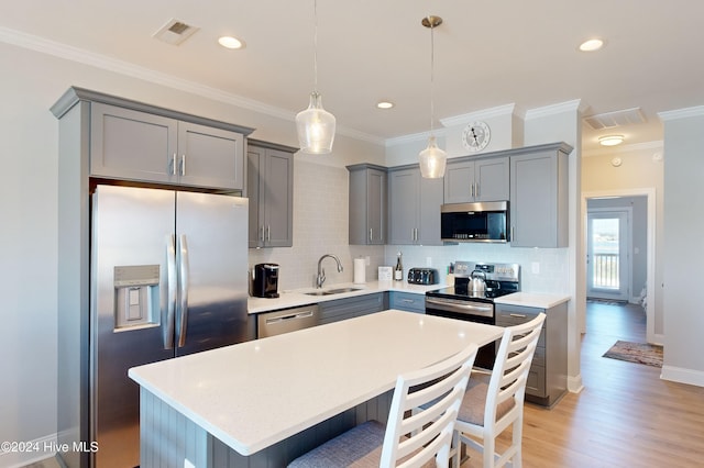 kitchen with ornamental molding, stainless steel appliances, hanging light fixtures, and light hardwood / wood-style floors