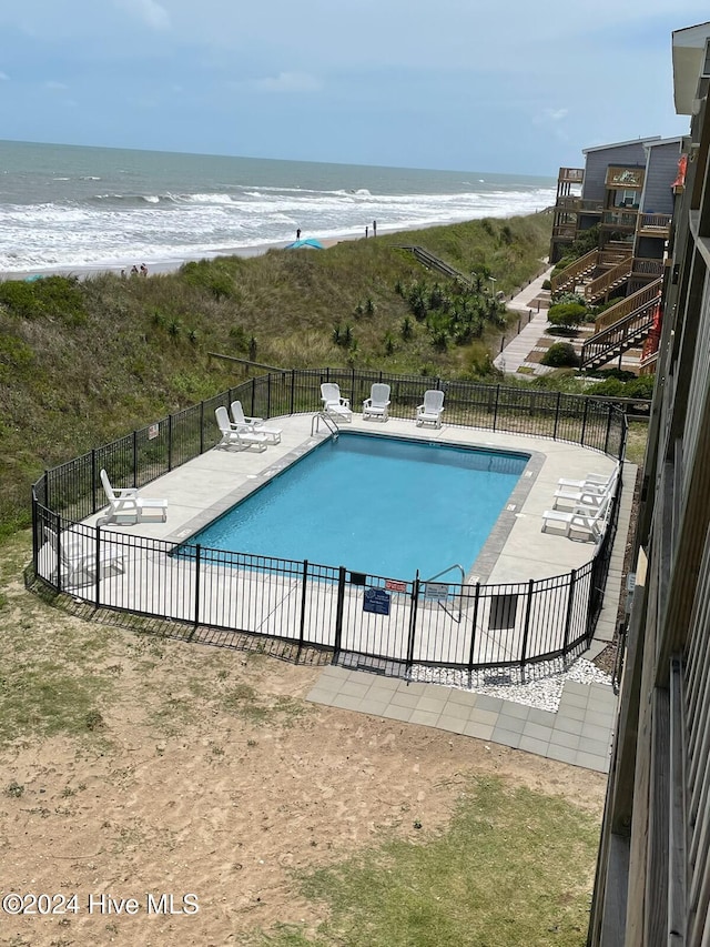 view of swimming pool with a patio area, a water view, and a beach view