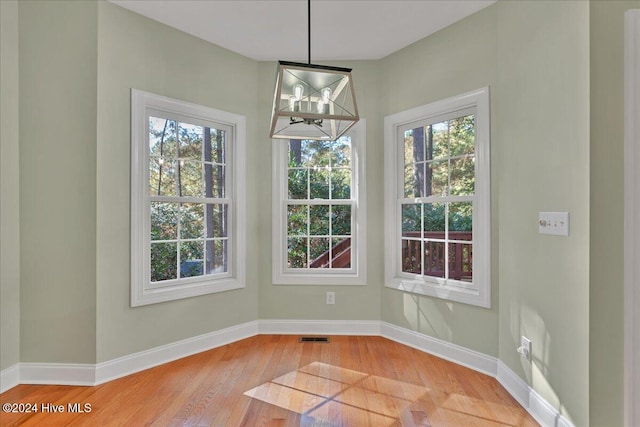 unfurnished dining area with hardwood / wood-style flooring, a healthy amount of sunlight, and a notable chandelier