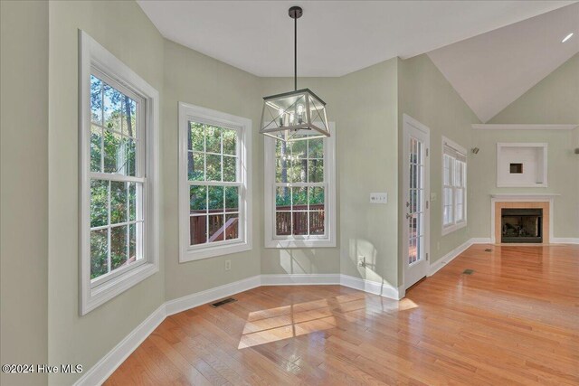 unfurnished dining area featuring light hardwood / wood-style floors, a tile fireplace, lofted ceiling, and a notable chandelier