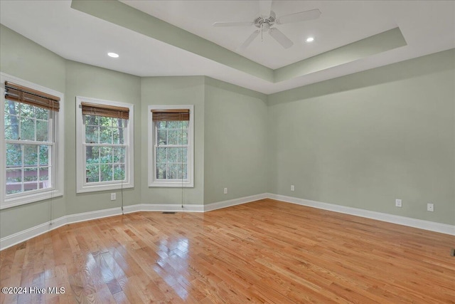 spare room with ceiling fan, light wood-type flooring, and a tray ceiling