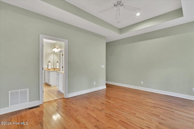 unfurnished room featuring light wood-type flooring, ceiling fan, and a tray ceiling