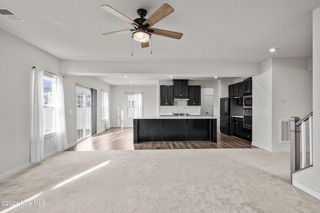 kitchen with appliances with stainless steel finishes, a textured ceiling, ceiling fan, a center island with sink, and carpet floors