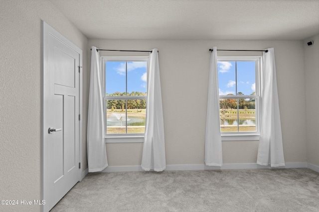 carpeted spare room featuring a textured ceiling and a water view