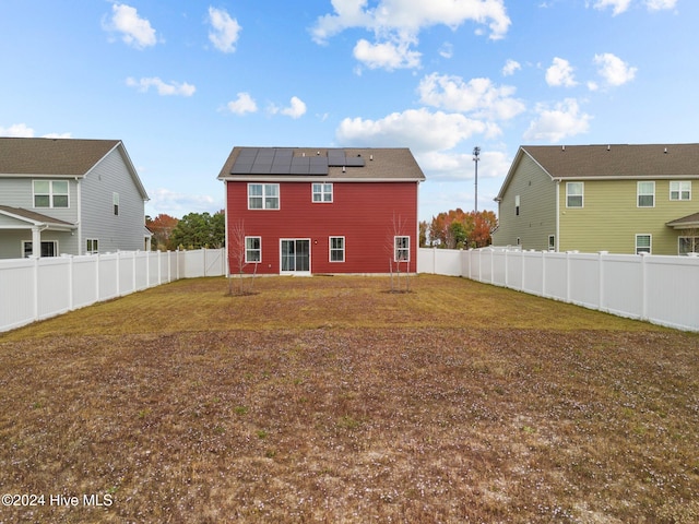 back of property with solar panels and a yard