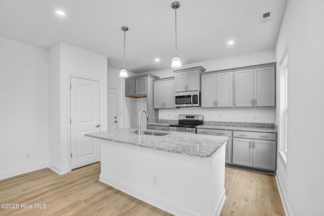 kitchen featuring appliances with stainless steel finishes, an island with sink, sink, light stone counters, and light wood-type flooring