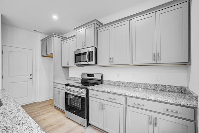 kitchen featuring stainless steel appliances, light stone countertops, gray cabinetry, and light hardwood / wood-style flooring