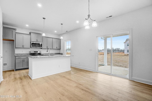 kitchen featuring stainless steel appliances, gray cabinetry, a center island with sink, and decorative light fixtures