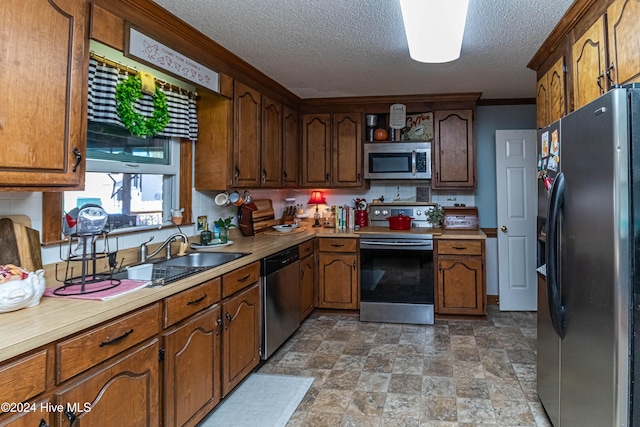 kitchen featuring a textured ceiling, sink, appliances with stainless steel finishes, and crown molding