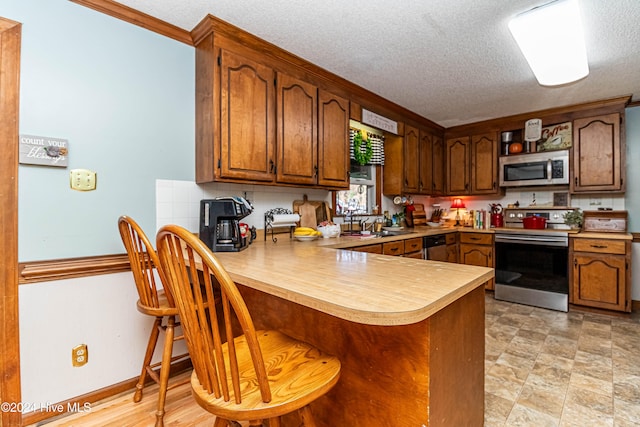 kitchen with stainless steel appliances, kitchen peninsula, tasteful backsplash, a textured ceiling, and crown molding