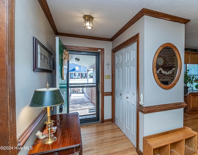 entryway with ornamental molding, light wood-type flooring, and a textured ceiling