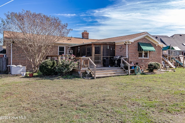 rear view of property featuring a sunroom, a lawn, and a wooden deck