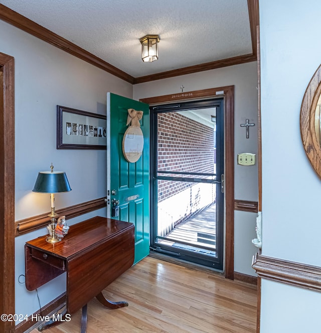 entryway with light wood-type flooring, a textured ceiling, and ornamental molding