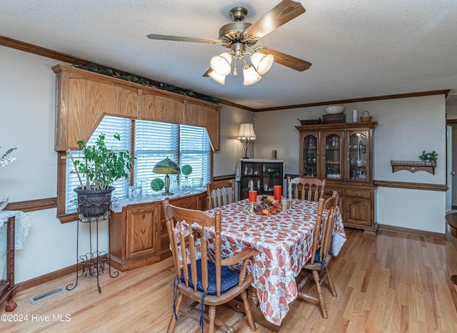 dining space featuring a textured ceiling, light wood-type flooring, ornamental molding, and ceiling fan