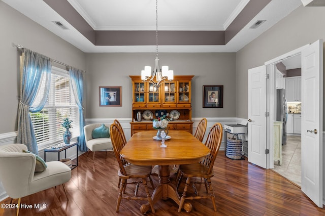 dining area featuring an inviting chandelier, a tray ceiling, crown molding, and dark wood-type flooring