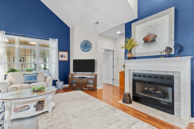 living room with lofted ceiling, wood-type flooring, and a tiled fireplace