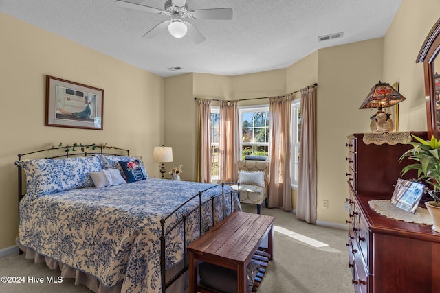 bedroom featuring ceiling fan, light colored carpet, and a textured ceiling