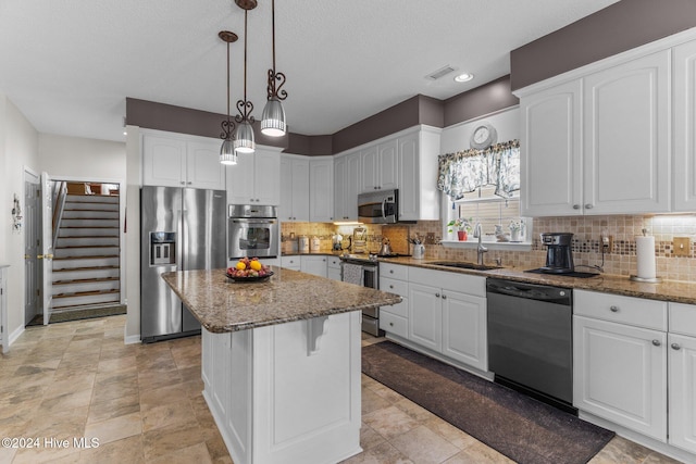 kitchen with appliances with stainless steel finishes, sink, pendant lighting, stone countertops, and a center island