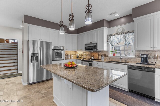 kitchen with white cabinets, a kitchen island, hanging light fixtures, and appliances with stainless steel finishes