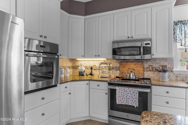 kitchen with dark stone countertops, white cabinetry, stainless steel appliances, and decorative backsplash