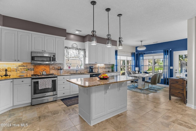 kitchen featuring white cabinets, light stone countertops, hanging light fixtures, and appliances with stainless steel finishes