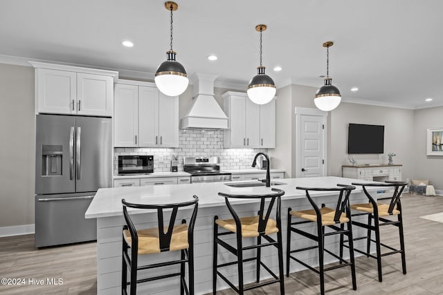 kitchen featuring light wood-type flooring, premium range hood, stainless steel appliances, and a kitchen island with sink