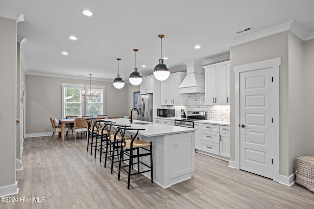 kitchen with a center island with sink, light wood-type flooring, custom range hood, and stainless steel appliances