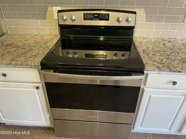 room details with white cabinets, decorative backsplash, light stone counters, and stainless steel range with electric cooktop