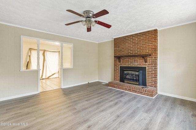 unfurnished living room featuring ceiling fan, a textured ceiling, crown molding, a brick fireplace, and light wood-type flooring