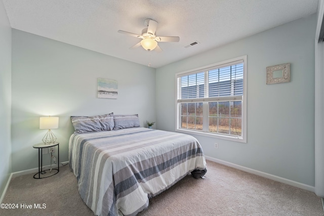 bedroom with ceiling fan, light colored carpet, and a textured ceiling