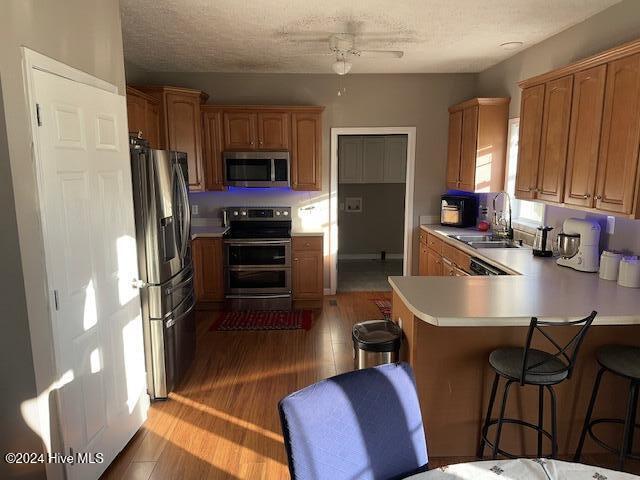 kitchen with wood-type flooring, kitchen peninsula, sink, a kitchen breakfast bar, and appliances with stainless steel finishes