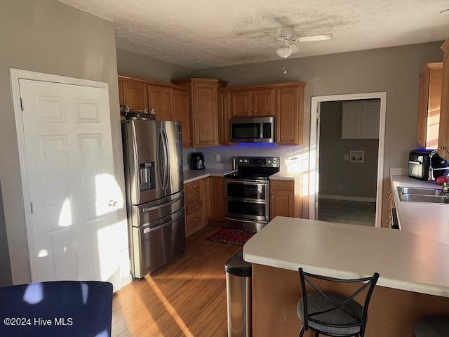 kitchen with stainless steel appliances, sink, kitchen peninsula, ceiling fan, and light hardwood / wood-style flooring