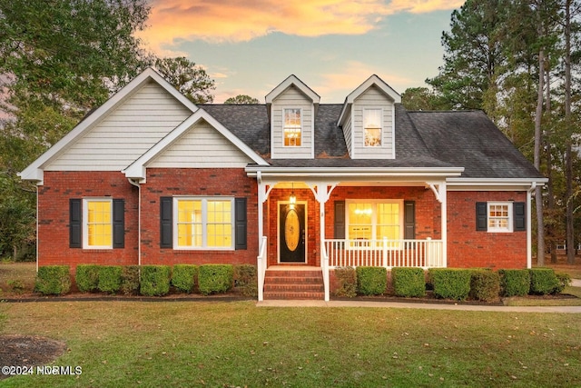 cape cod home with covered porch and a yard