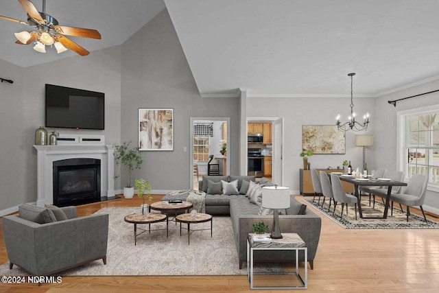 living room with ceiling fan with notable chandelier, crown molding, light hardwood / wood-style flooring, and vaulted ceiling