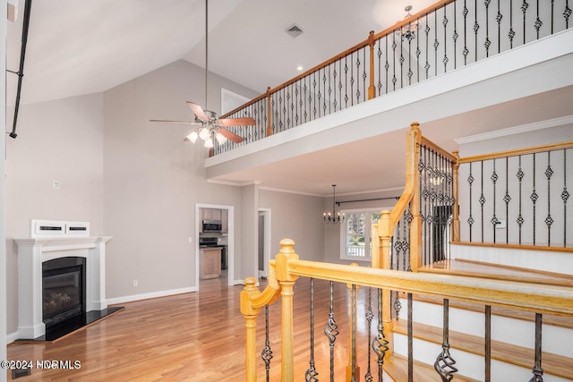 stairs with high vaulted ceiling, ceiling fan with notable chandelier, wood-type flooring, and crown molding