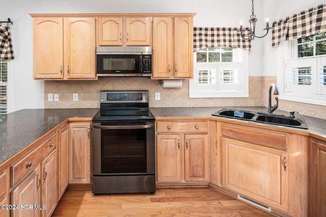 kitchen with stainless steel appliances, a notable chandelier, hanging light fixtures, sink, and light hardwood / wood-style floors