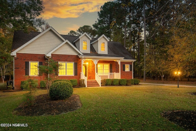 cape cod home with a lawn and covered porch