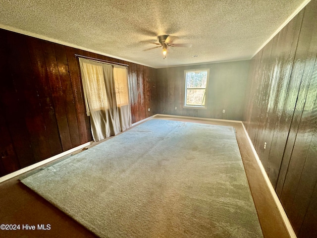 empty room featuring carpet flooring, a textured ceiling, wood walls, and ceiling fan