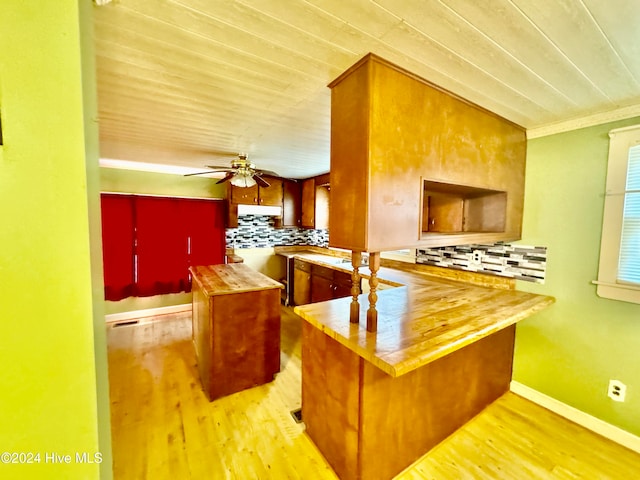 kitchen featuring butcher block counters, decorative backsplash, kitchen peninsula, crown molding, and light wood-type flooring