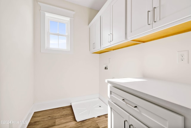 clothes washing area with hardwood / wood-style floors, hookup for a washing machine, and cabinets